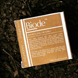 Biode Into The Sunset Shampoo Bar packaging resting on a dark natural ground, showing the back label and product details.