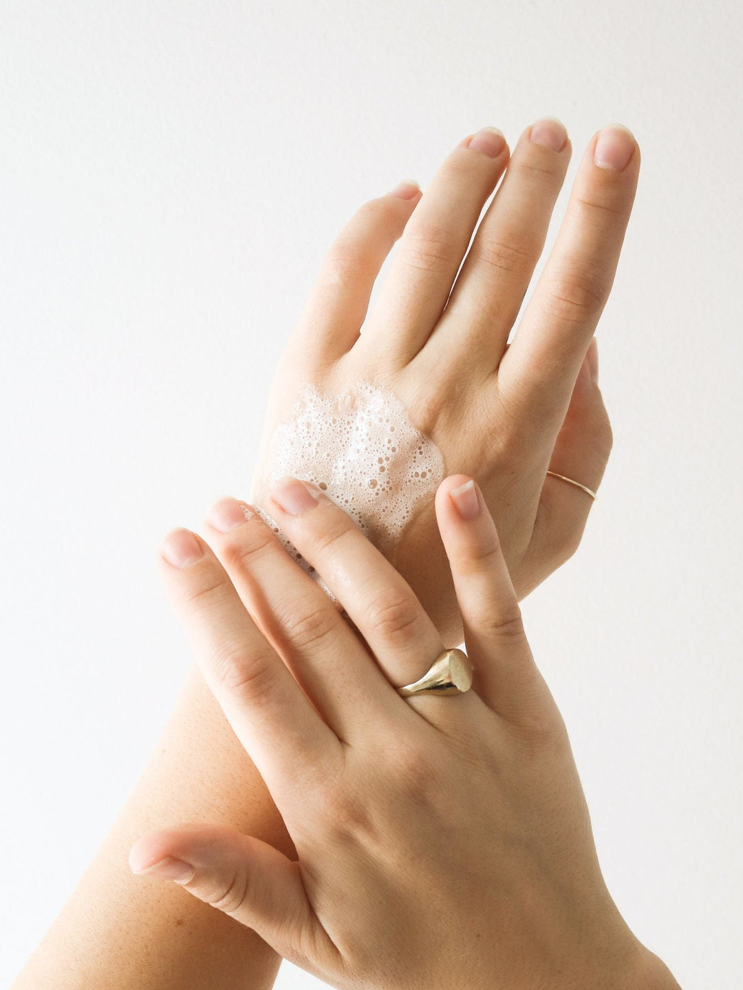 Close-up of hands spreading white cleanser foam over the back of a hand, demonstrating the lather of Biologi Bc Refresh Cleanser.