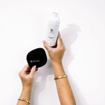 Hands hold Biologi Bc Refresh Cleanser and a round black Biologi cleansing mitt against white, showing a cleansing routine with the accessory.