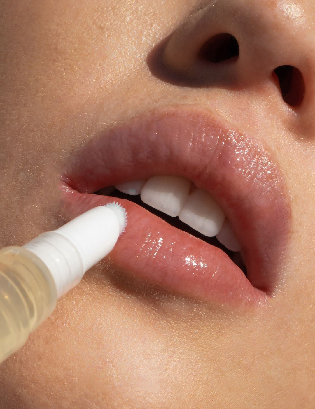 Close-up of the Biologi Bl Nourish Lip Serum brush applicator touching a woman's lower lip, showing the clear golden serum pen in use.