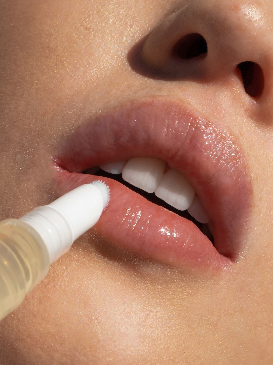 Close-up of the Biologi Bl Nourish Lip Serum brush applicator touching a woman's lower lip, showing the clear golden serum pen in use.