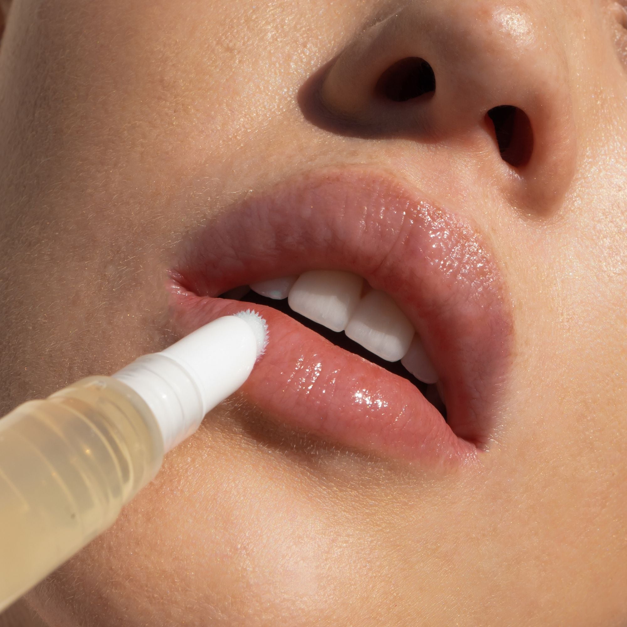 Close-up of the Biologi Bl Nourish Lip Serum brush applicator touching a woman's lower lip, showing the clear golden serum pen in use.