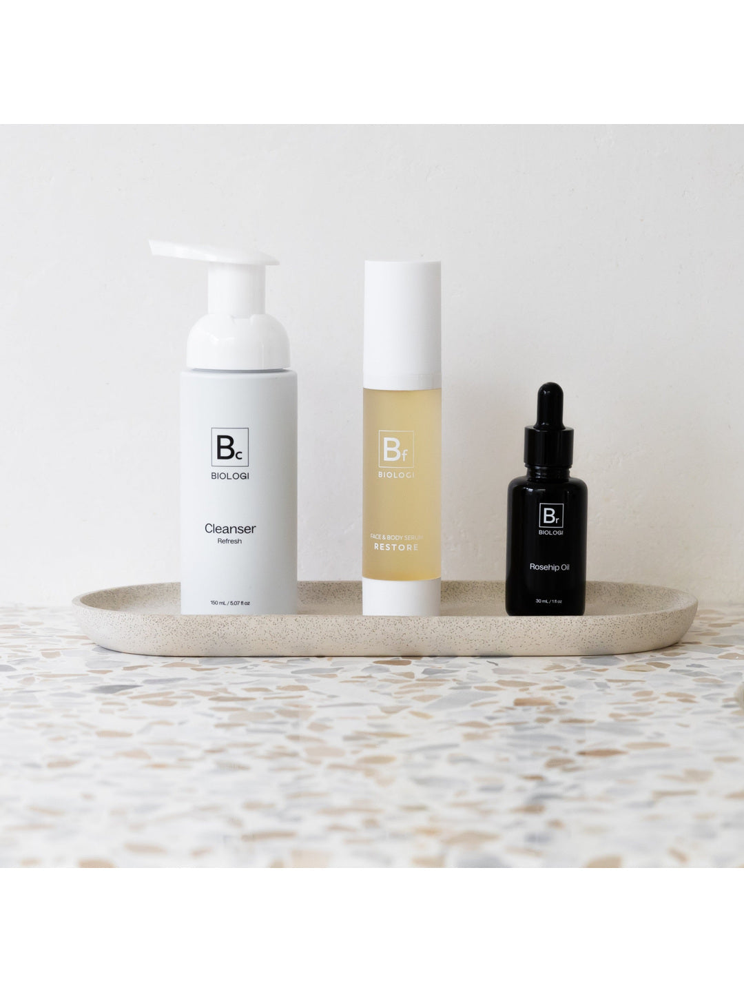 Biologi Bc Refresh Cleanser, Bf Restore serum and Br Rosehip Oil arranged together on a stone tray, showing the three products in a skincare routine.