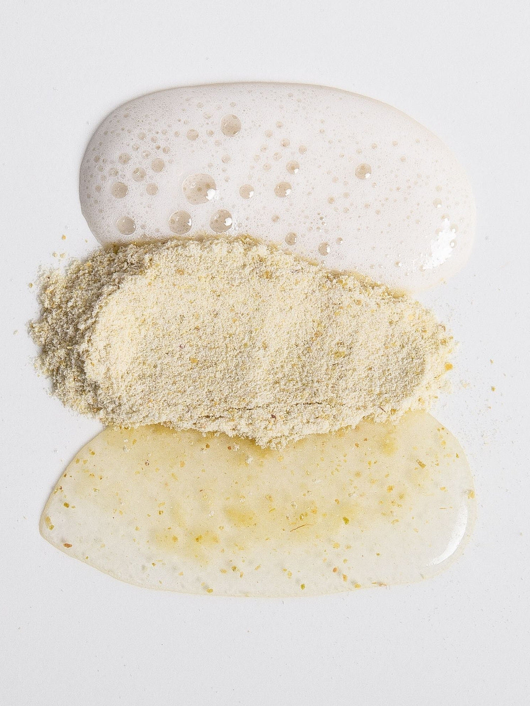 Biologi Bx Reveal Exfoliant powder between white cleanser foam and a golden mixed cream on a pale surface, showing the textures before and after mixing.