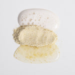 Biologi Bx Reveal Exfoliant powder between white cleanser foam and a golden mixed cream on a pale surface, showing the textures before and after mixing.