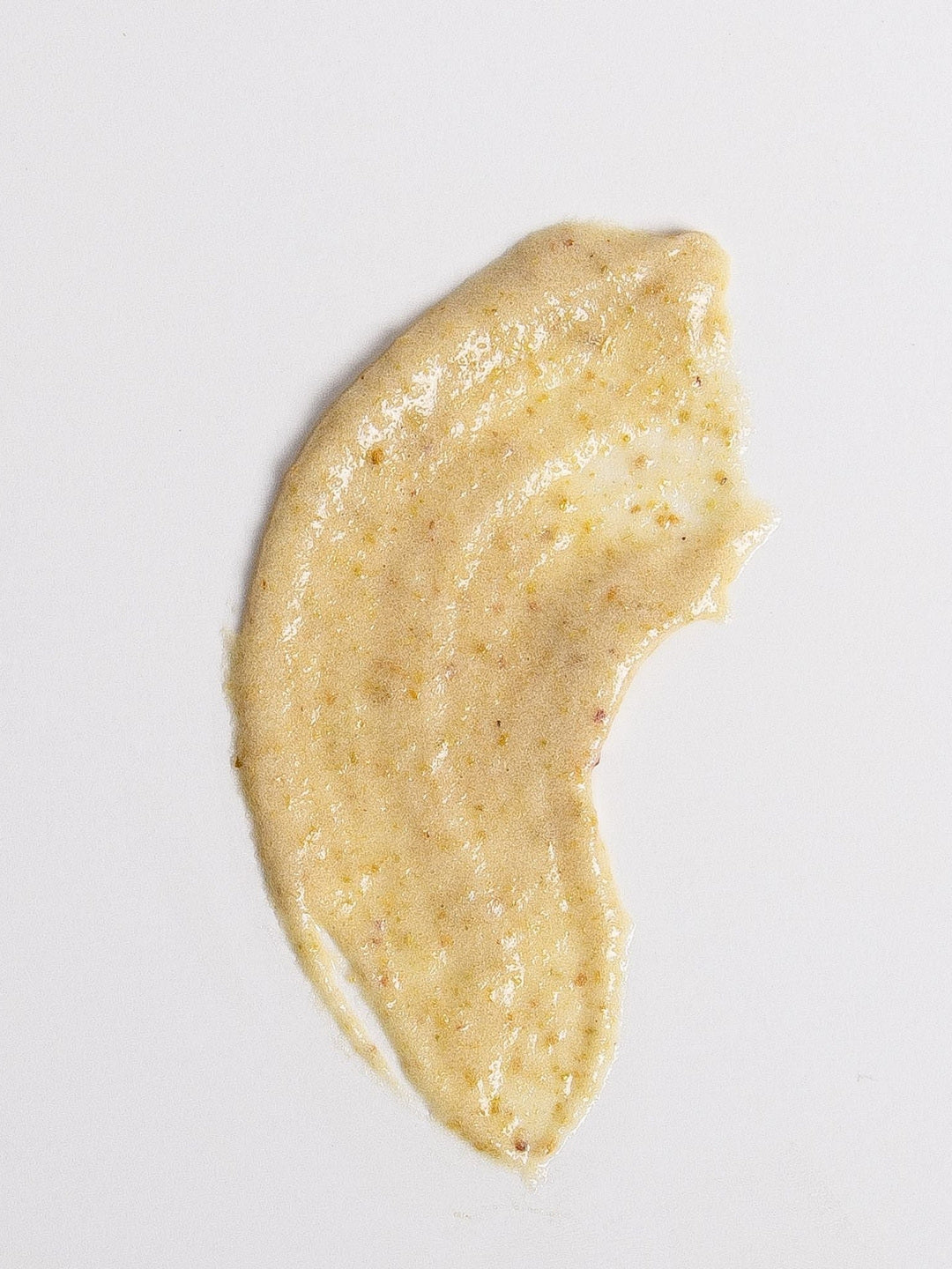 A curved smear of creamy golden Biologi Bx Reveal Exfoliant mixture on white, showing its fine granular texture.