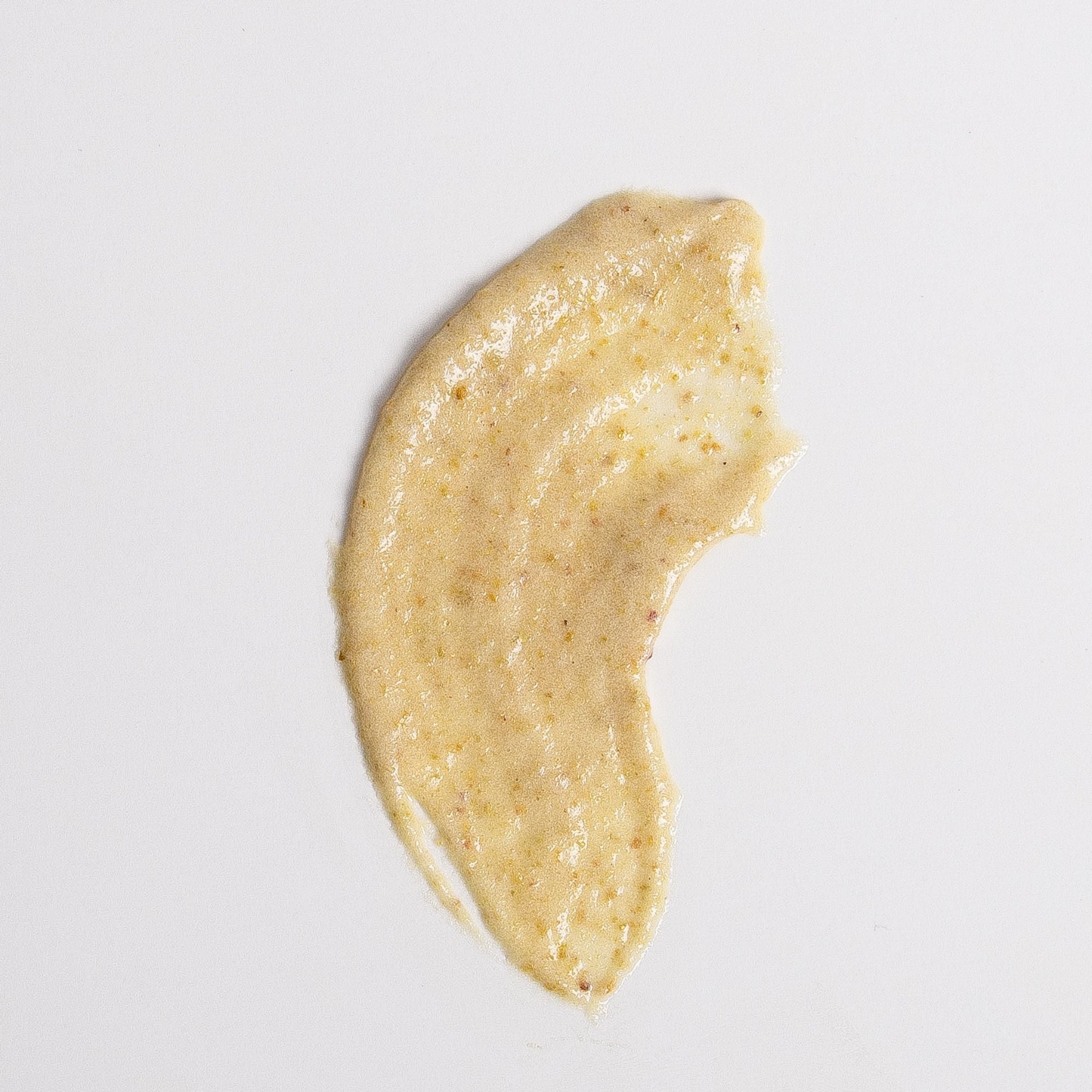 A curved smear of creamy golden Biologi Bx Reveal Exfoliant mixture on white, showing its fine granular texture.