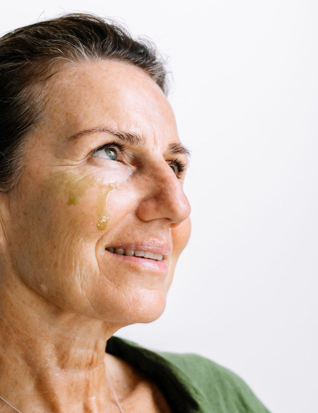 A woman looks to the side with golden Biologi By Blackberry Seed Oil visible on her cheek, showing the facial oil on skin.