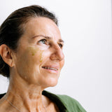 A woman looks to the side with golden Biologi By Blackberry Seed Oil visible on her cheek, showing the facial oil on skin.