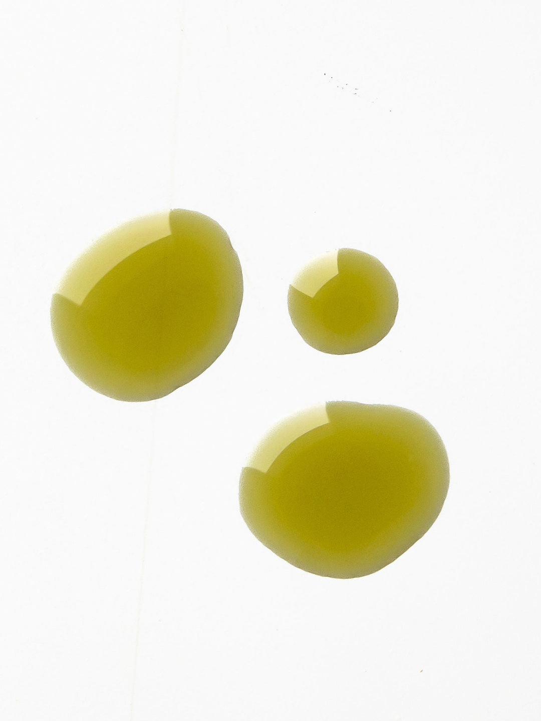 Three glossy golden-green drops of Biologi By Blackberry Seed Oil on a pale background, showing its colour and liquid texture.