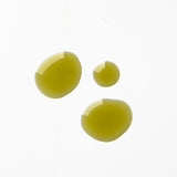 Three glossy golden-green drops of Biologi By Blackberry Seed Oil on a pale background, showing its colour and liquid texture.
