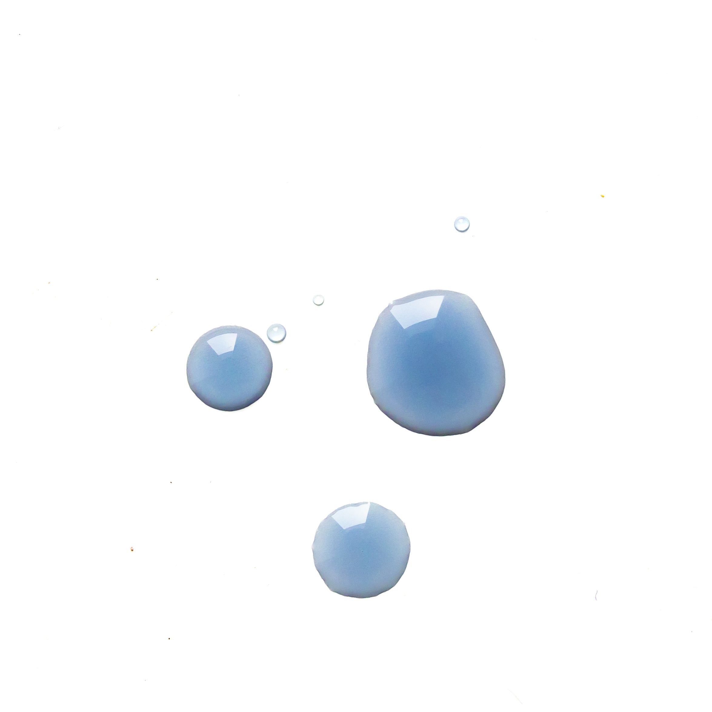 Three glossy blue-lavender drops of serum on white, illustrating the colour and fluid texture of Biologi Revive Bio Cellulose Eye Mask essence.