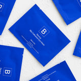 Several cobalt-blue Biologi Revive Bio Cellulose Eye Mask sachets arranged diagonally on a textured white fabric surface.