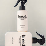 Two Breed Wee Spray Odour Neutralising bottles displayed upright and horizontally on a pale studio set.