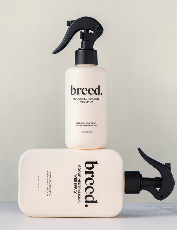 Two Breed Wee Spray Odour Neutralising bottles displayed upright and horizontally on a pale studio set.