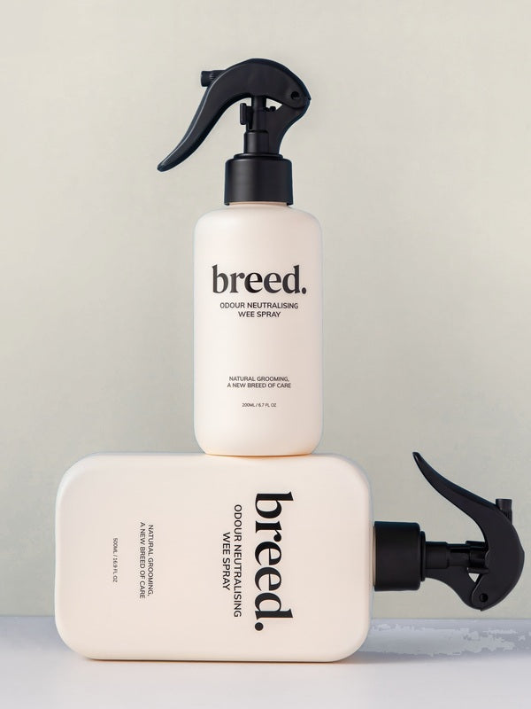Two Breed Wee Spray Odour Neutralising bottles displayed upright and horizontally on a pale studio set.