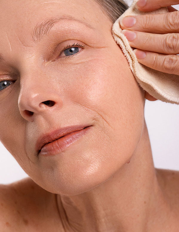 Woman wiping her cheek with a soft cloth while cleansing with Ere Perez Ginkgo Micellar Cleanser