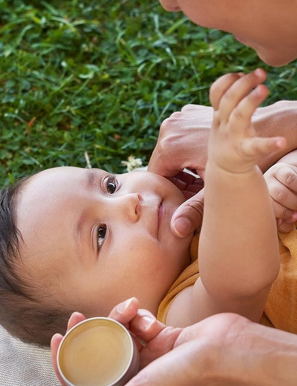 Weleda Calendula All Purpose Balm held beside a baby