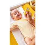 Smiling baby wearing yellow, lying down and being applied Calendula Face Cream on his face.