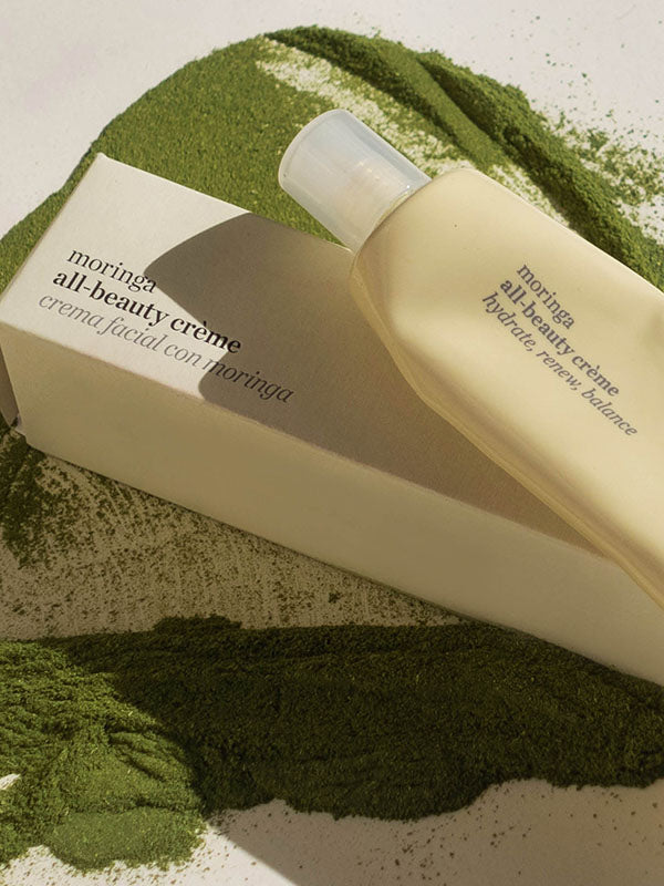 Ere Perez Moringa All-Beauty Creme tube and box resting on green moringa powder