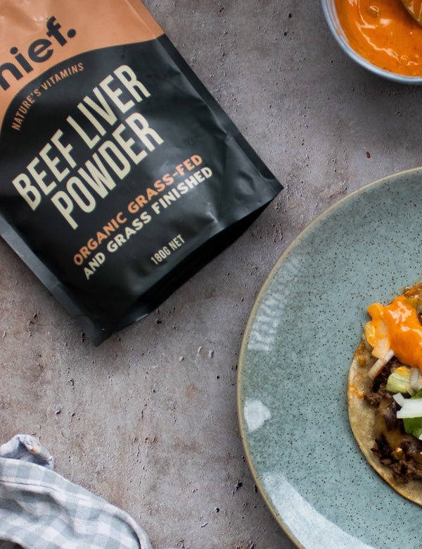 Chief Beef Liver Powder pouch beside a blue-grey plate holding a round tortilla topped with browned filling, chopped vegetables and orange sauce.