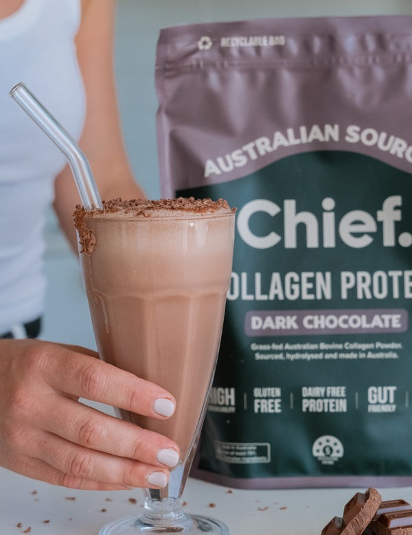 Hand holding a chocolate collagen drink beside CHIEF Collagen Protein