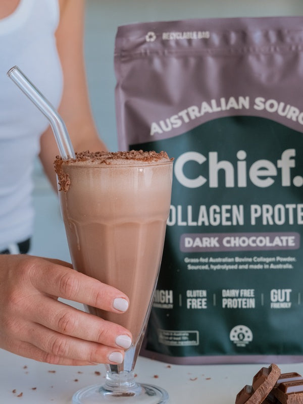 Hand holding a chocolate collagen drink beside CHIEF Collagen Protein