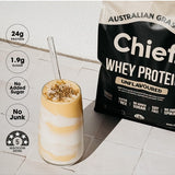 Tall layered pale yellow and white shake topped with granola beside a Chief Unflavoured Whey Protein pouch. Graphic badges state 24g protein, 1.9g sugar, no added sugar, no junk and a five-star health rating.