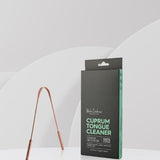 U-shaped copper tongue scraper standing beside its tall black and mint-green carton on a white ledge against a pale grey background.