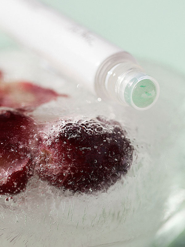 Ere Perez Grape Water Eye Serum rollerball frozen in ice with grapes on a mint background