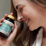 Smiling woman holding the Herbs of Gold Clear Skin bottle beside her cheek