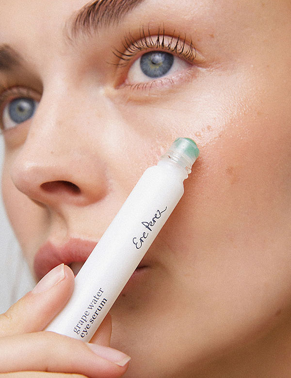 Young woman rolling Ere Perez Grape Water Eye Serum onto the skin under her eye