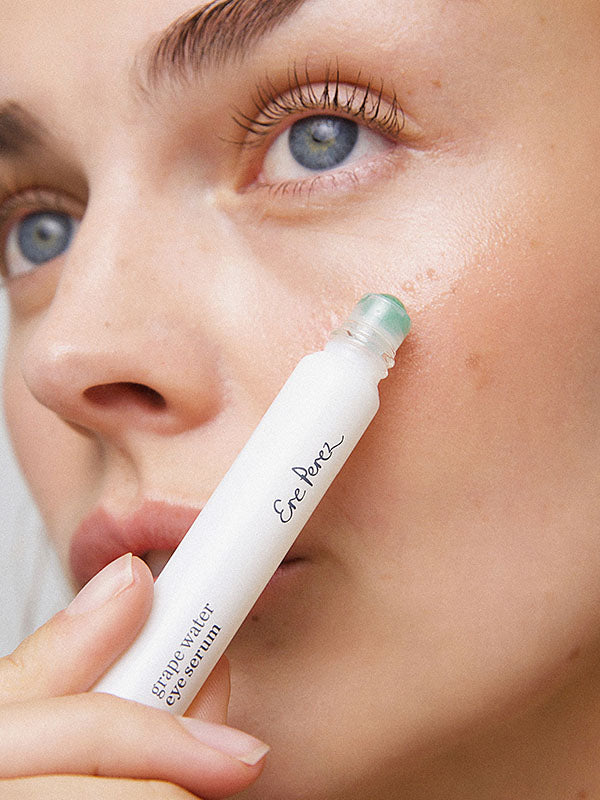 Young woman rolling Ere Perez Grape Water Eye Serum onto the skin under her eye