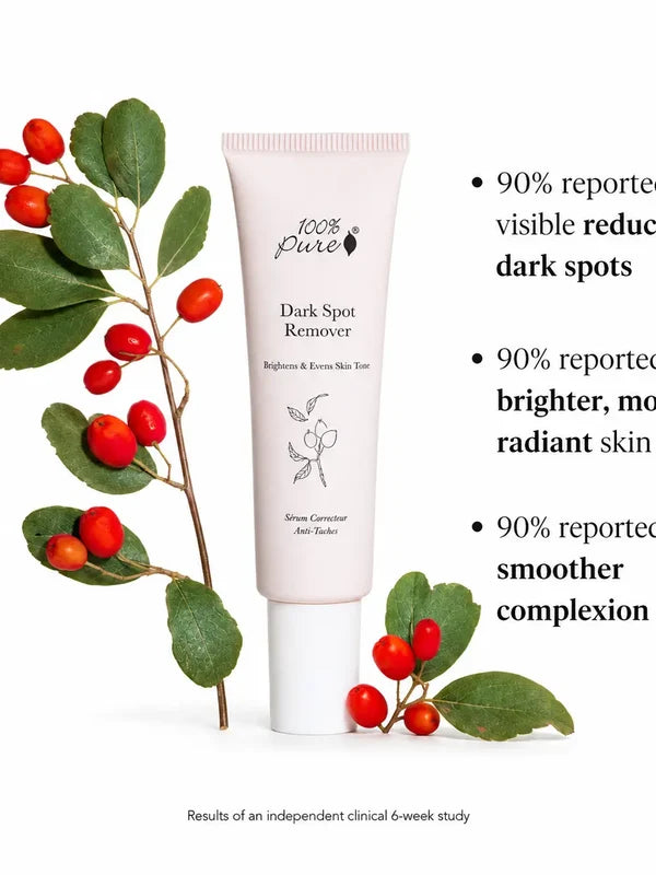 A pale pink 100% Pure Dark Spot Remover tube stands beside green leaves and red berries. Partly cropped text lists three 90% study results about dark spots, brighter skin and a smoother complexion, with a six-week-study footnote.