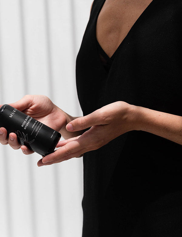 Woman in a black dress holding the Mukti Botanique Natural Deodorant Sandalwood and Sage