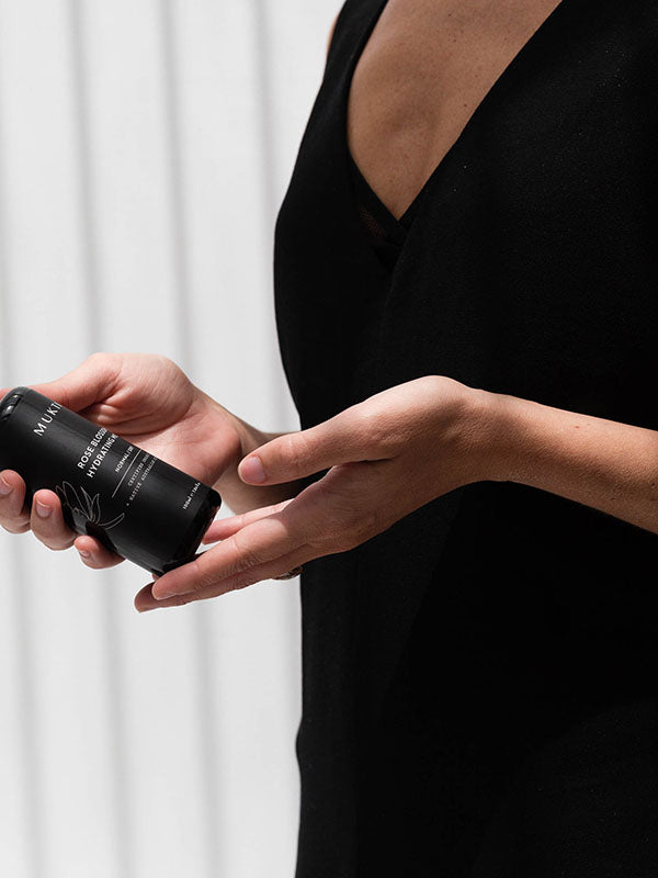 Woman in a black dress holding the Mukti Botanique Natural Deodorant Sandalwood and Sage