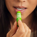Close-up of a woman applying Dr. Bronner's Lemon Lime Lip Balm to her lower lip from a bright green tube.