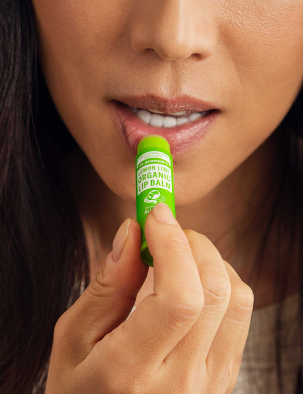 Close-up of a woman applying Dr. Bronner's Lemon Lime Lip Balm to her lower lip from a bright green tube.
