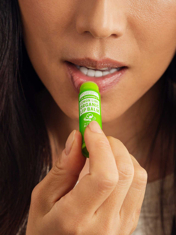 Close-up of a woman applying Dr. Bronner's Lemon Lime Lip Balm to her lower lip from a bright green tube.