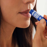 Close-up of a woman applying Dr. Bronner's Peppermint Lip Balm from a dark blue tube to the edge of her lips.