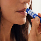 Close-up of a woman applying Dr. Bronner's Peppermint Lip Balm from a dark blue tube to the edge of her lips.