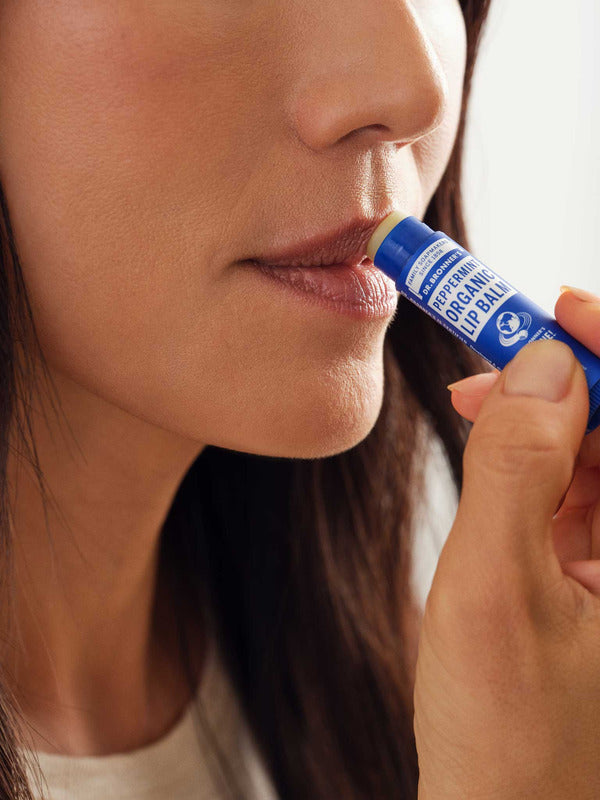 Close-up of a woman applying Dr. Bronner's Peppermint Lip Balm from a dark blue tube to the edge of her lips.