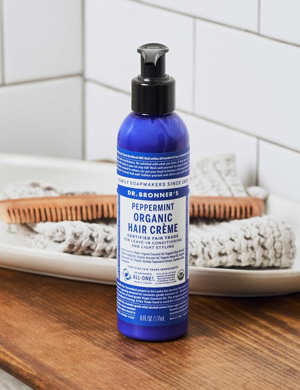 Dr. Bronner's Peppermint Leave In Conditioner bottle displayed on a bathroom counter with hair brushes.
