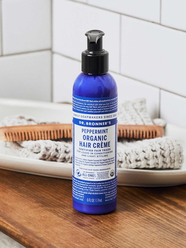 Dr. Bronner's Peppermint Leave In Conditioner bottle displayed on a bathroom counter with hair brushes.