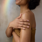 A person wrapped in a brown waffle towel smoothing lotion over their shoulder and upper arm, the body application photograph from Dr. Bronner's Peppermint Organic Lotion page.