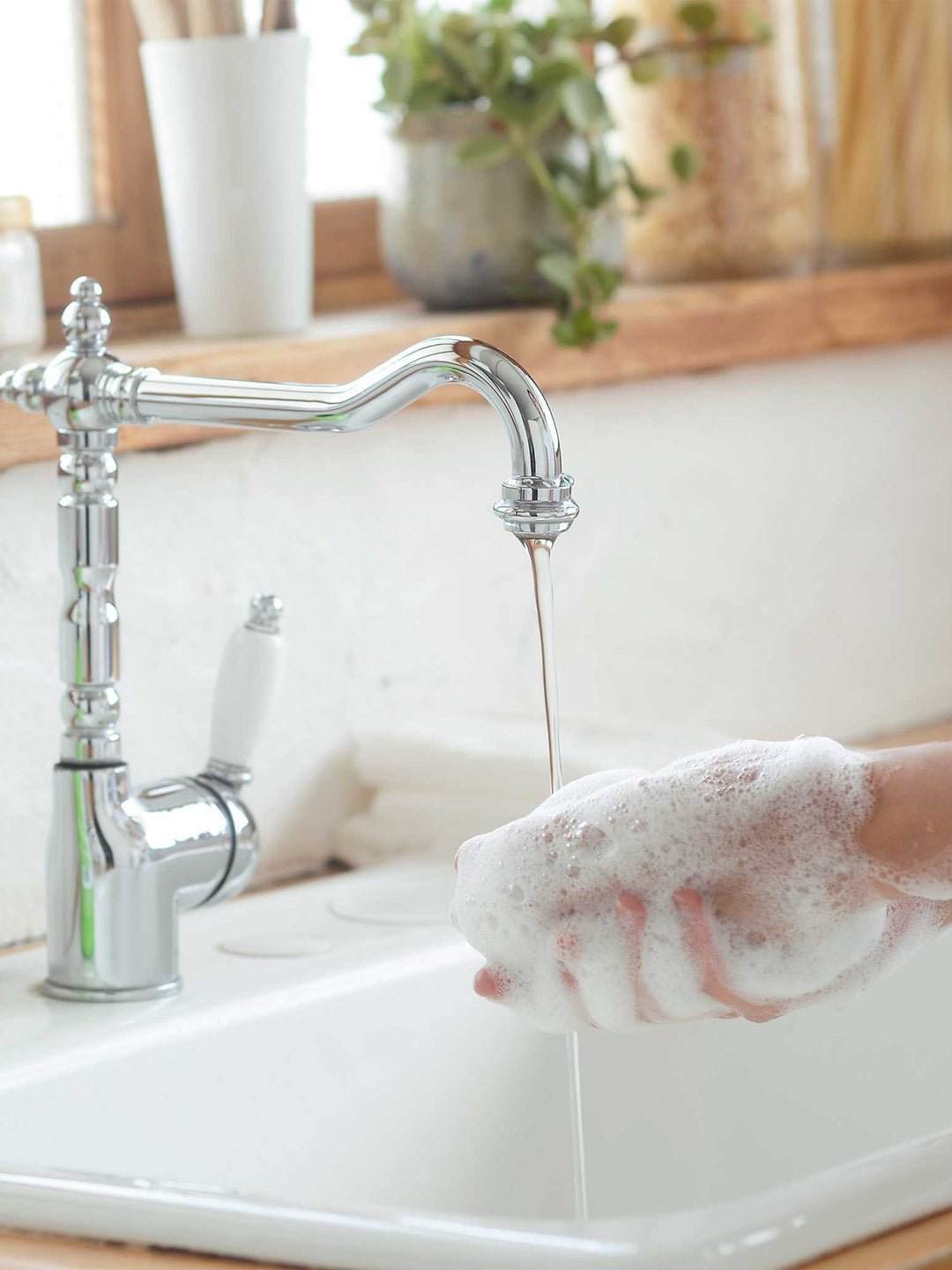 Close-up of hands covered in a thick white soap lather beside a running chrome tap, the hand-washing image from Dr. Bronner's Lavender Organic Sugar Soap page.