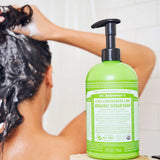 Rear view of a person lathering their wet hair in the shower, beside a green Dr. Bronner's Lemongrass Lime Organic Sugar Soap 710ml pump bottle in the foreground.