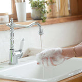 Close-up of hands covered in white soap lather beside a running chrome tap, the hand-washing image from Dr. Bronner's Tea Tree Organic Sugar Soap page.