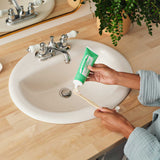 Hands squeezing toothpaste from a green Dr. Bronner's Spearmint tube onto a wooden toothbrush above a white bathroom basin.