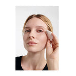 Woman holding a white cotton pad against the outer corner of her eye while removing eye makeup.
